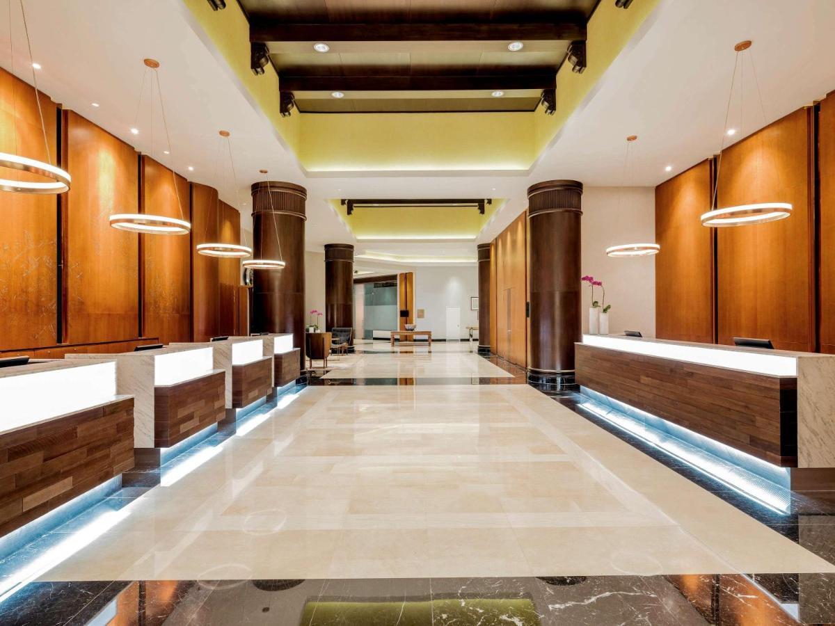 Paradox Singapore Merchant Court At Clarke Quay المظهر الخارجي الصورة The photo shows a spacious and modern hotel lobby. It features several reception desks arranged along one side, each with a sleek, illuminated design. The walls are finished in warm wooden tones, and there are pendant lights hanging from the ceiling,