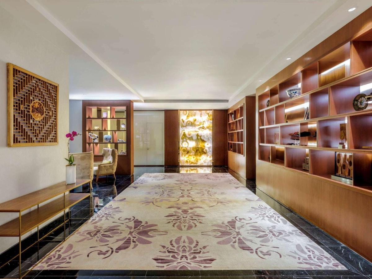 Paradox Singapore Merchant Court At Clarke Quay المظهر الخارجي الصورة The photo shows a sleek and modern interior space, likely a lobby or lounge area. The floor is adorned with a large, elegant rug featuring floral patterns in soft colors. On one side, there is a wooden shelf filled with decorative items and books, al