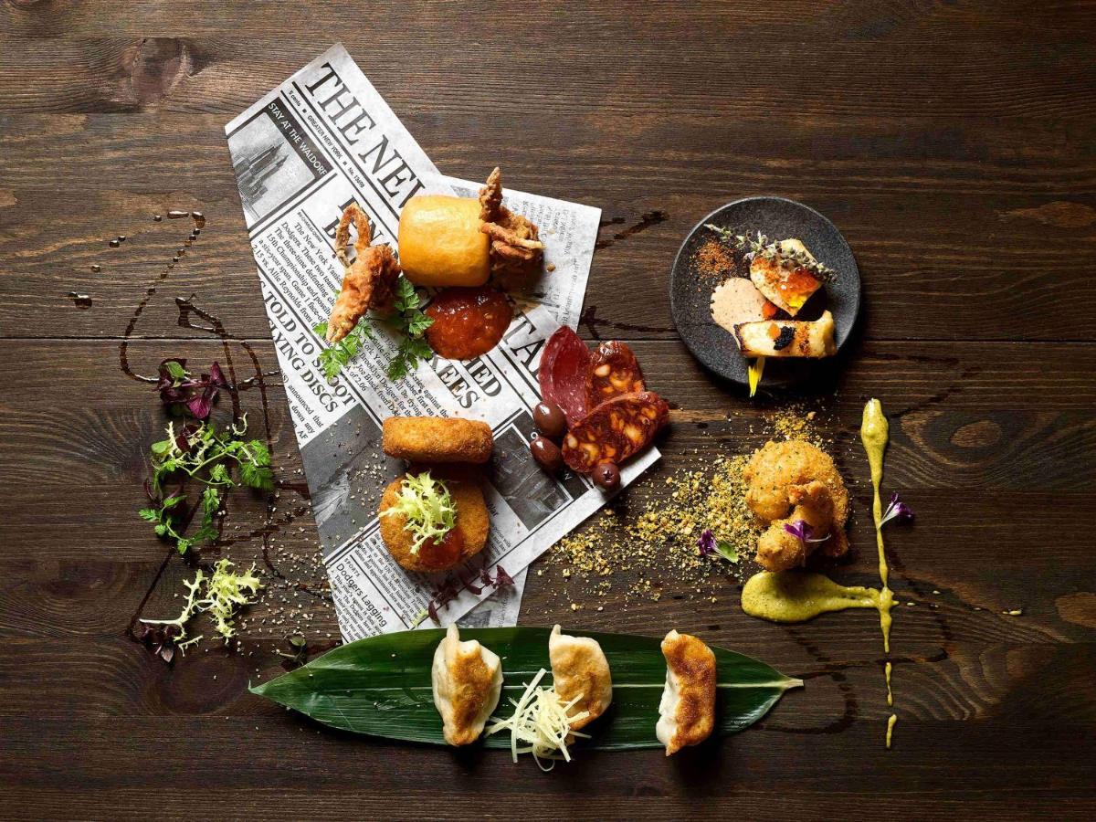 Paradox Singapore Merchant Court At Clarke Quay المظهر الخارجي الصورة The photo displays an artistic arrangement of various food items on a dark wooden table. The food is positioned atop a crumpled newspaper, creating a casual yet sophisticated dining presentation. 

There are several pieces of fried food, including wh
