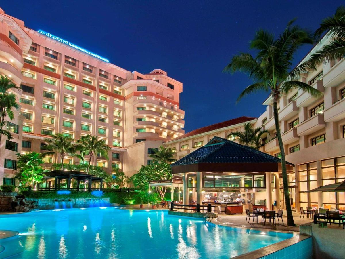 Paradox Singapore Merchant Court At Clarke Quay المظهر الخارجي الصورة The photo depicts a luxurious hotel complex set against a twilight sky. In the foreground, there is a large swimming pool that reflects the light from surrounding lights and the sky. Lush greenery, including palm trees, adds to the tropical ambiance.