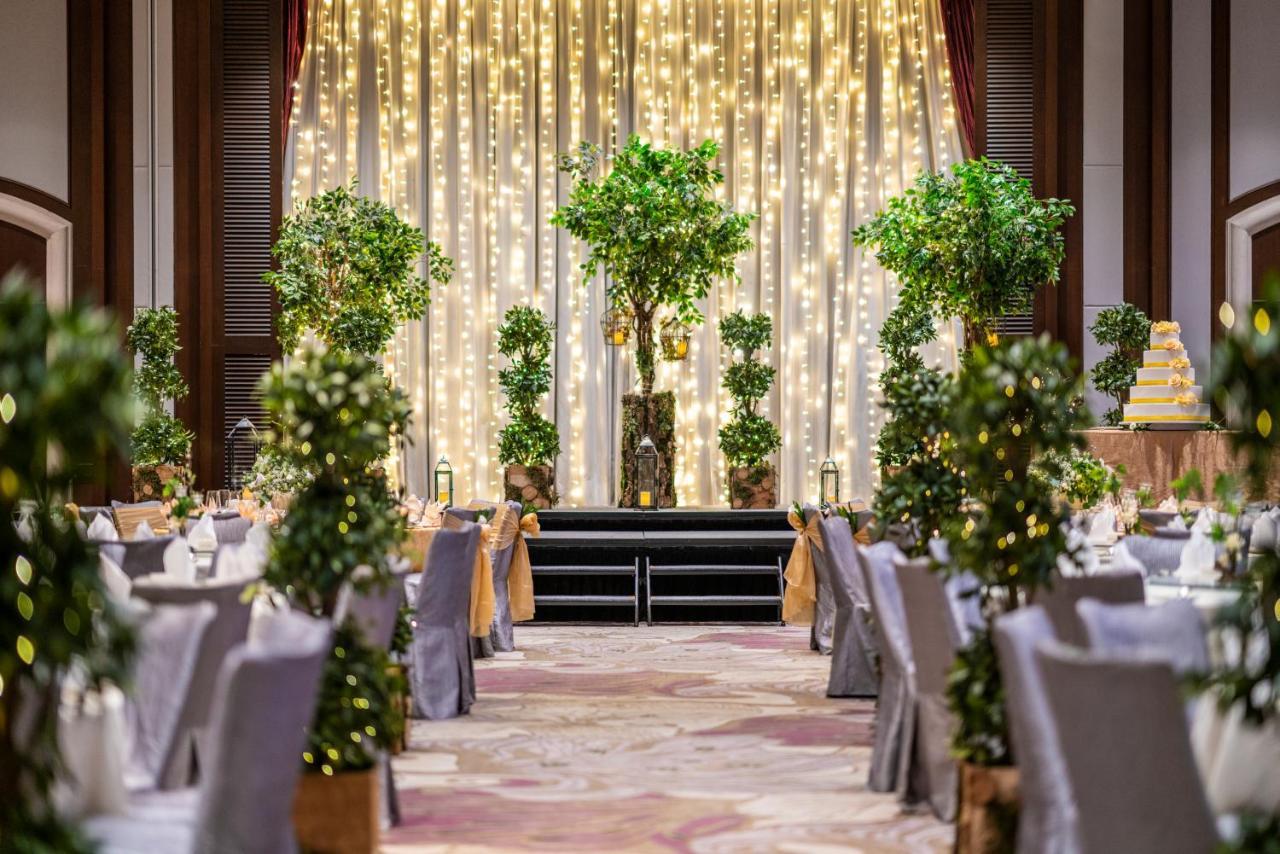 Paradox Singapore Merchant Court At Clarke Quay المظهر الخارجي الصورة The image shows an elegantly decorated event space, likely for a wedding or formal celebration. In the center, there is a backdrop with draped fabric illuminated by soft lights, creating a warm ambiance. There are several decorative trees or potted p