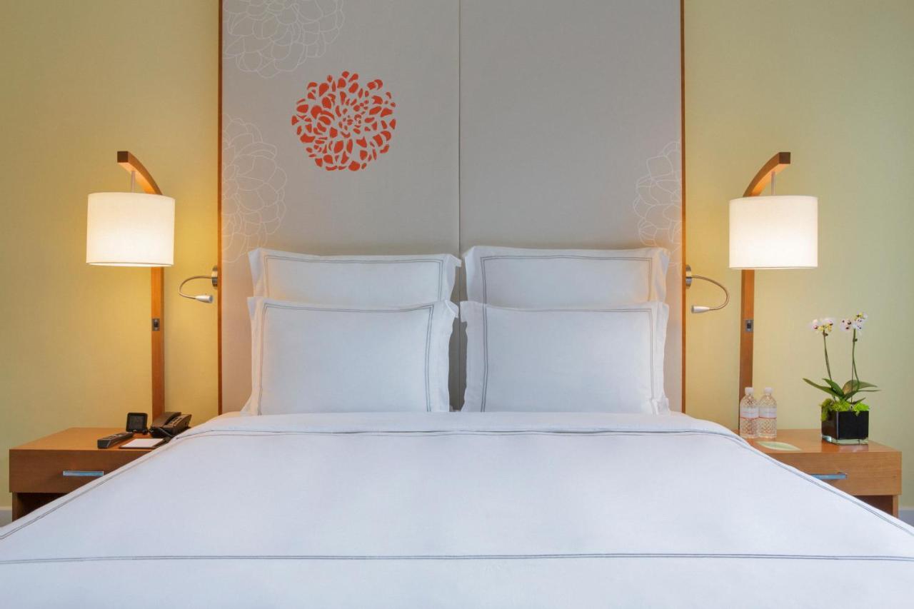 Paradox Singapore Merchant Court At Clarke Quay المظهر الخارجي الصورة The photo showcases a cozy hotel room with a neatly made bed featuring white linens and two pillows. Behind the bed is a decorative headboard with a simple floral design in orange. On either side of the bed, there are stylish bedside lamps providing 