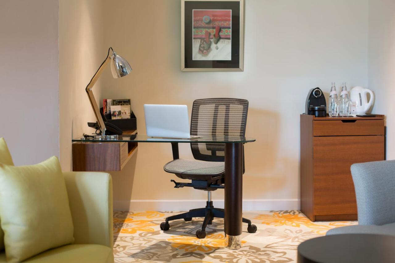 Paradox Singapore Merchant Court At Clarke Quay المظهر الخارجي الصورة The photo shows a workspace setup in a well-lit room. It features a modern desk with a glass top and a comfortable office chair. On the desk, there is a laptop and a desk lamp for illumination. To the side, there are some accessories and a coffee mac