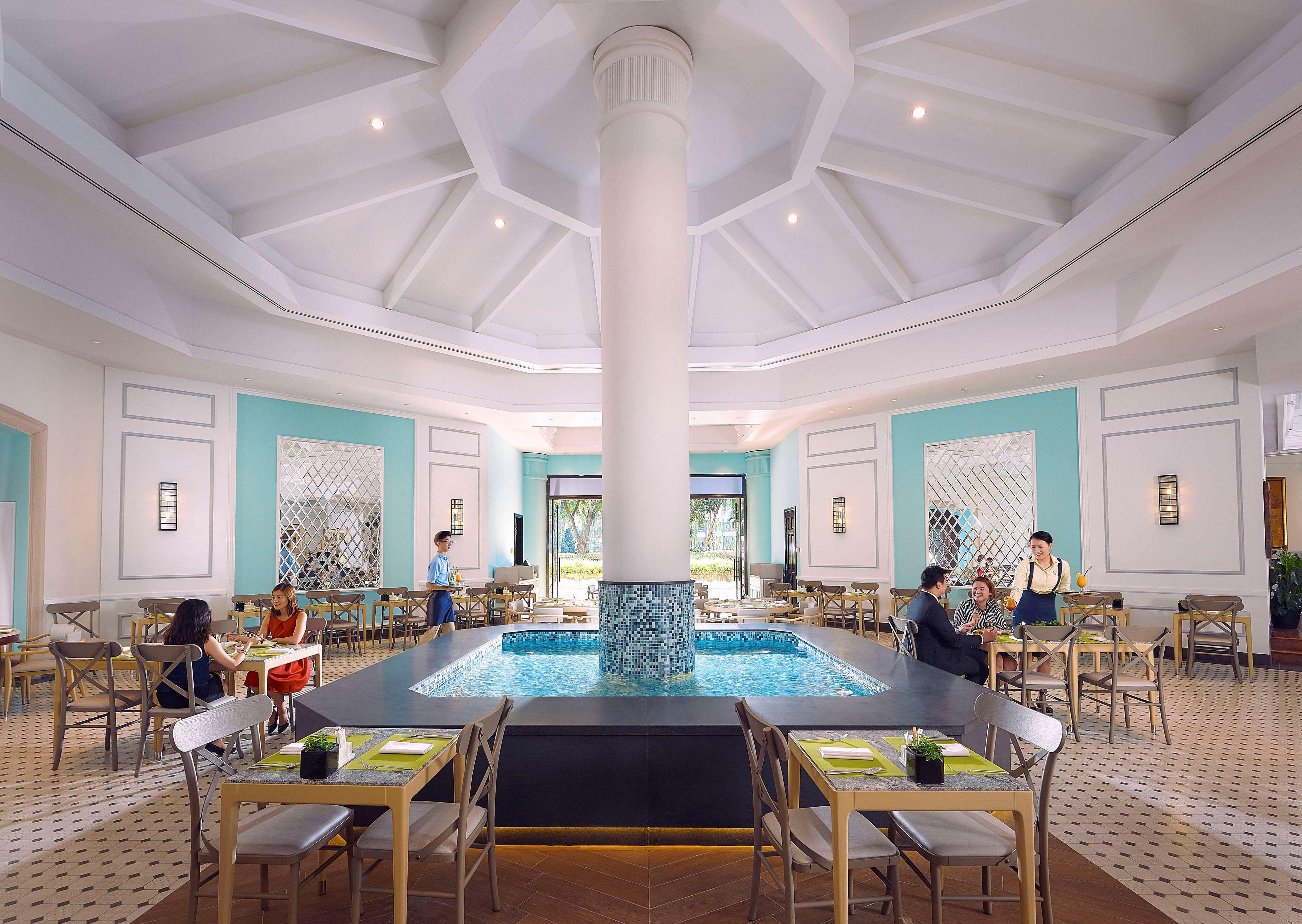 Paradox Singapore Merchant Court At Clarke Quay المظهر الخارجي الصورة The photo depicts an elegant restaurant interior characterized by a spacious, well-lit design. At the center, there is a large, round column that supports a high, intricately designed ceiling. Surrounding the column is a small pool of water, adding a