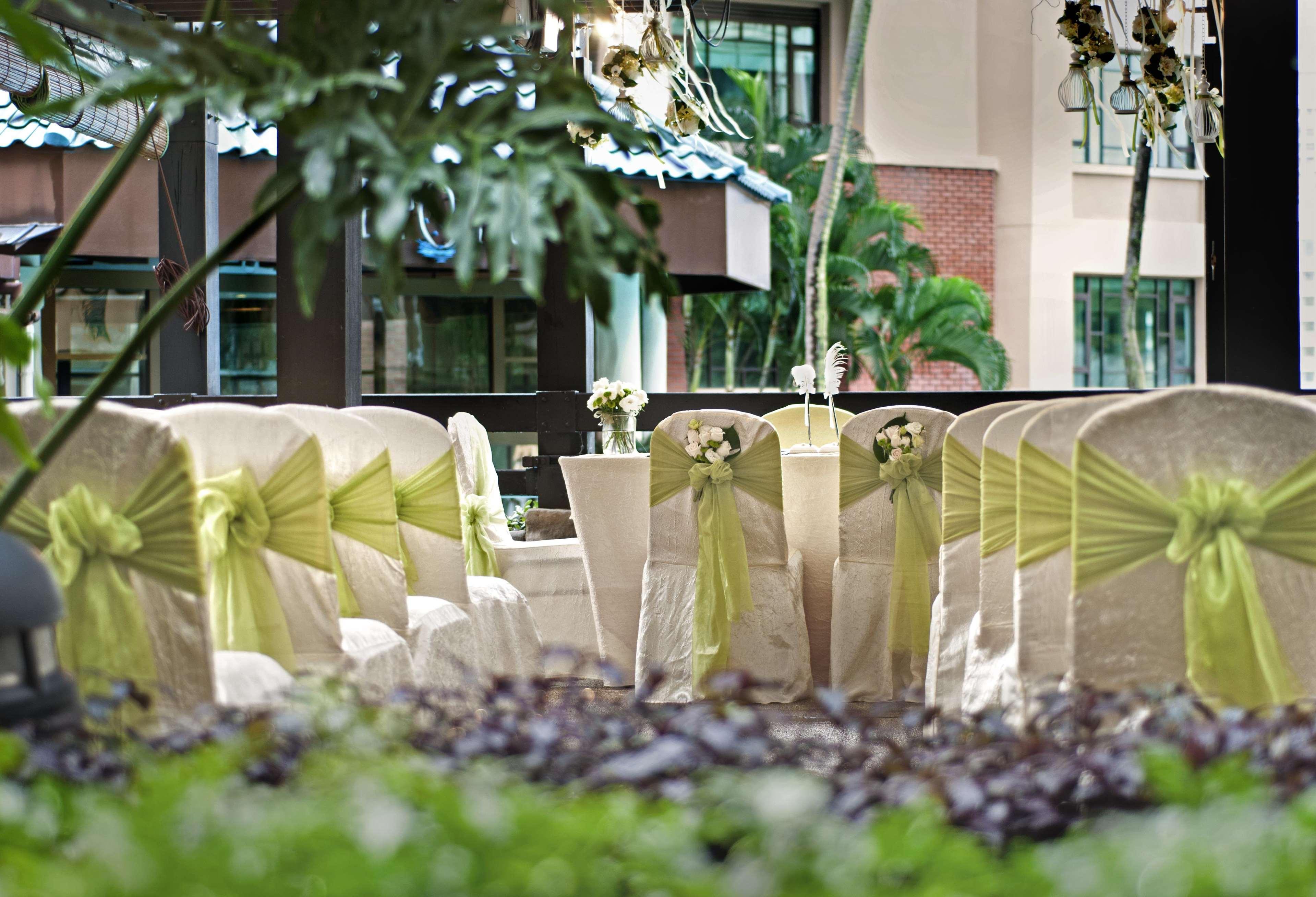 Paradox Singapore Merchant Court At Clarke Quay المظهر الخارجي الصورة The photo shows a decorated setting for an event, likely a wedding or a formal gathering. There are several chairs covered in light fabric with green sashes tied around them, creating an elegant look. In the foreground, there are potted plants and gr