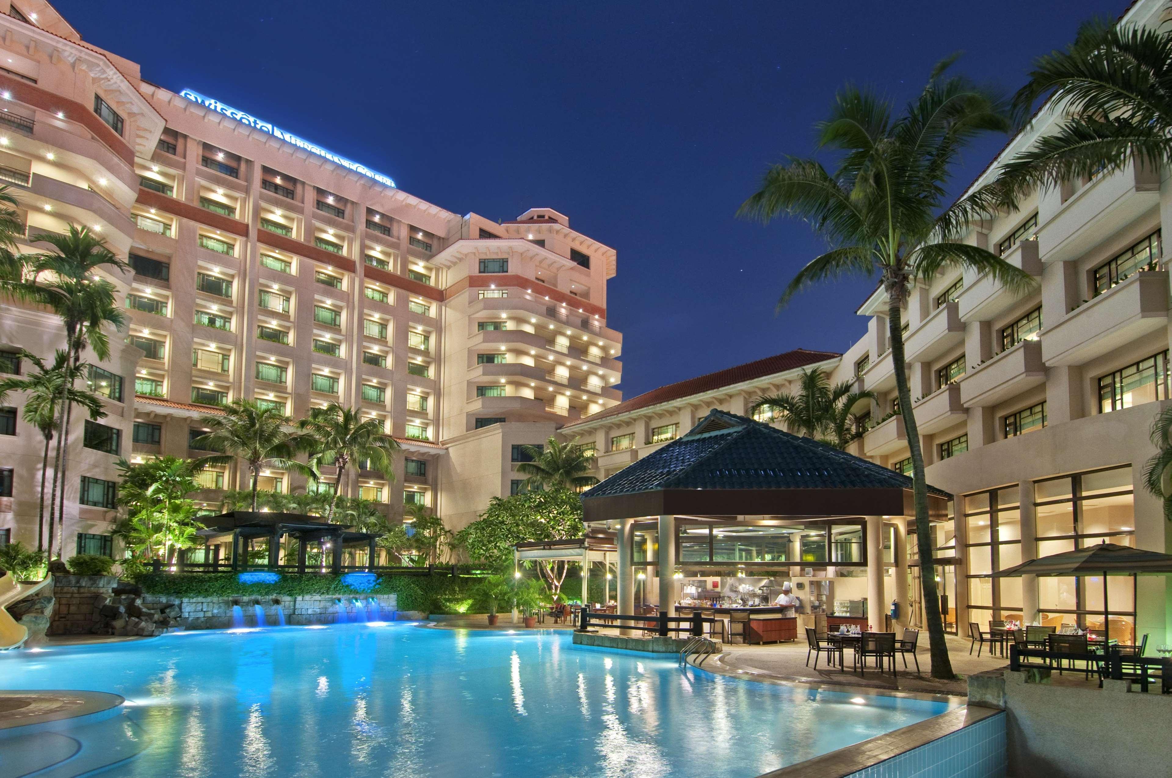 Paradox Singapore Merchant Court At Clarke Quay المرافق الصورة The photo depicts a modern hotel complex at night. The hotel buildings are illuminated, showcasing their architectural features. In the foreground, there is a large swimming pool, which reflects the lights from the surrounding area, creating a tranqu