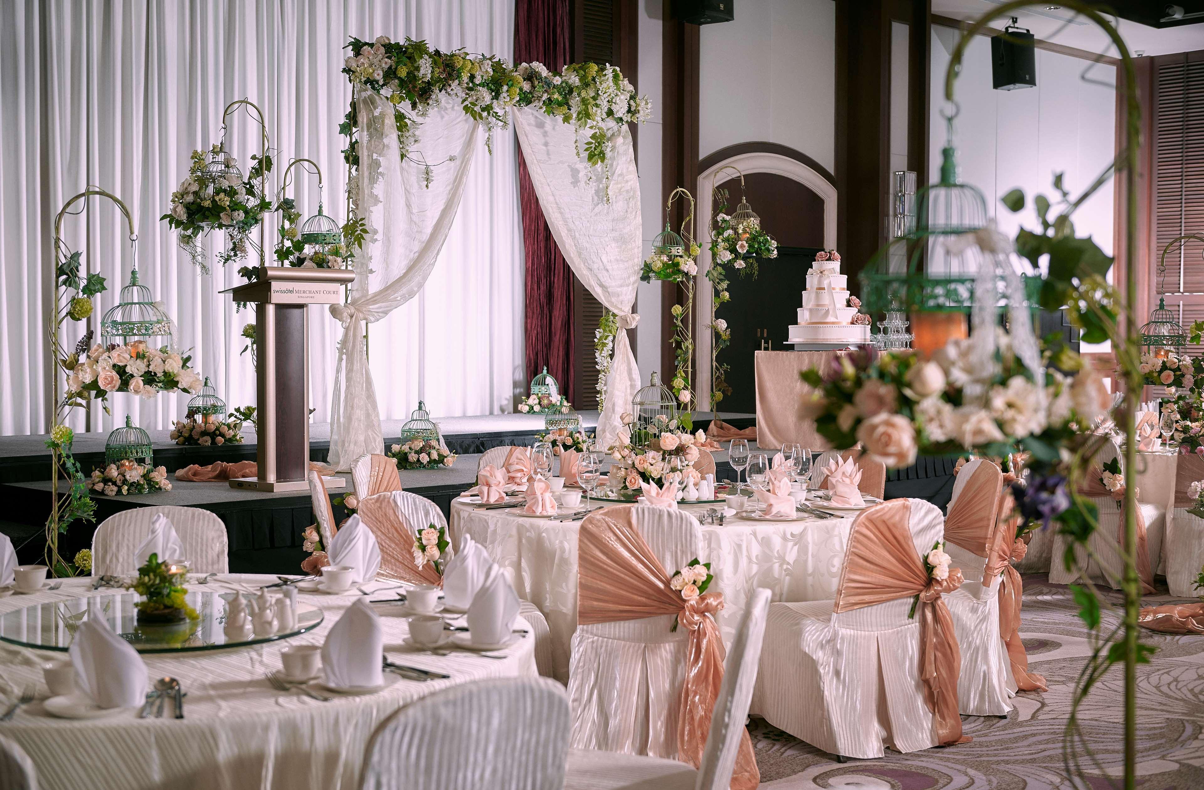 Paradox Singapore Merchant Court At Clarke Quay المظهر الخارجي الصورة The photo shows an elegantly decorated indoor event space, likely set up for a wedding or a formal celebration. There are several round tables covered with white tablecloths, each adorned with floral arrangements and cloth napkins. The chairs are dre
