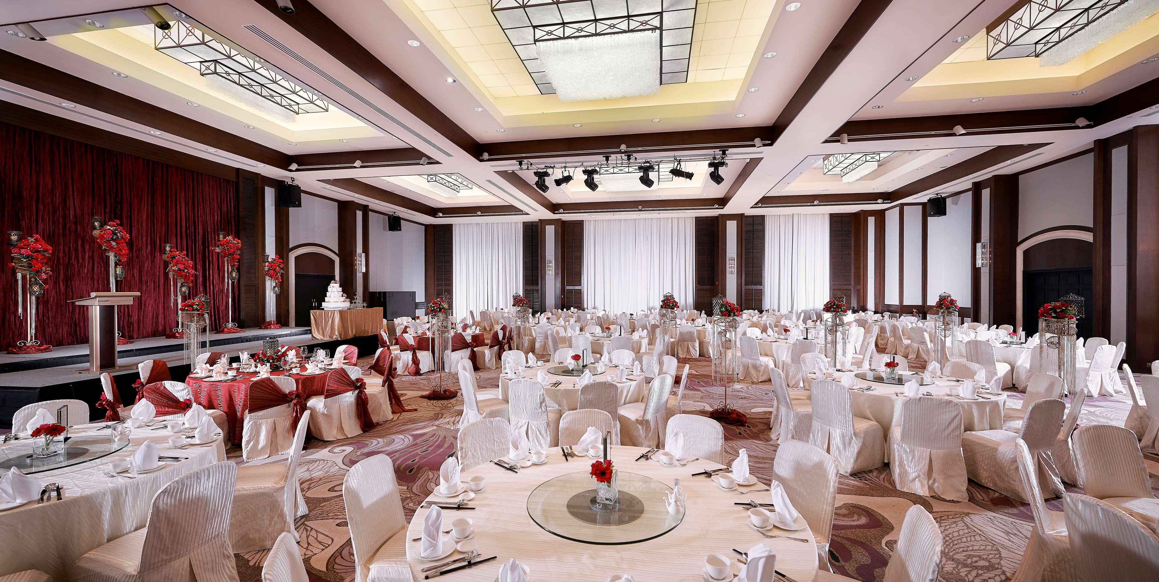 Paradox Singapore Merchant Court At Clarke Quay المظهر الخارجي الصورة The photo shows a spacious banquet hall set up for an elegant event. Round tables are beautifully arranged, each covered with a tablecloth and adorned with a center decoration featuring red flowers. The chairs are draped in white covers, adding to th