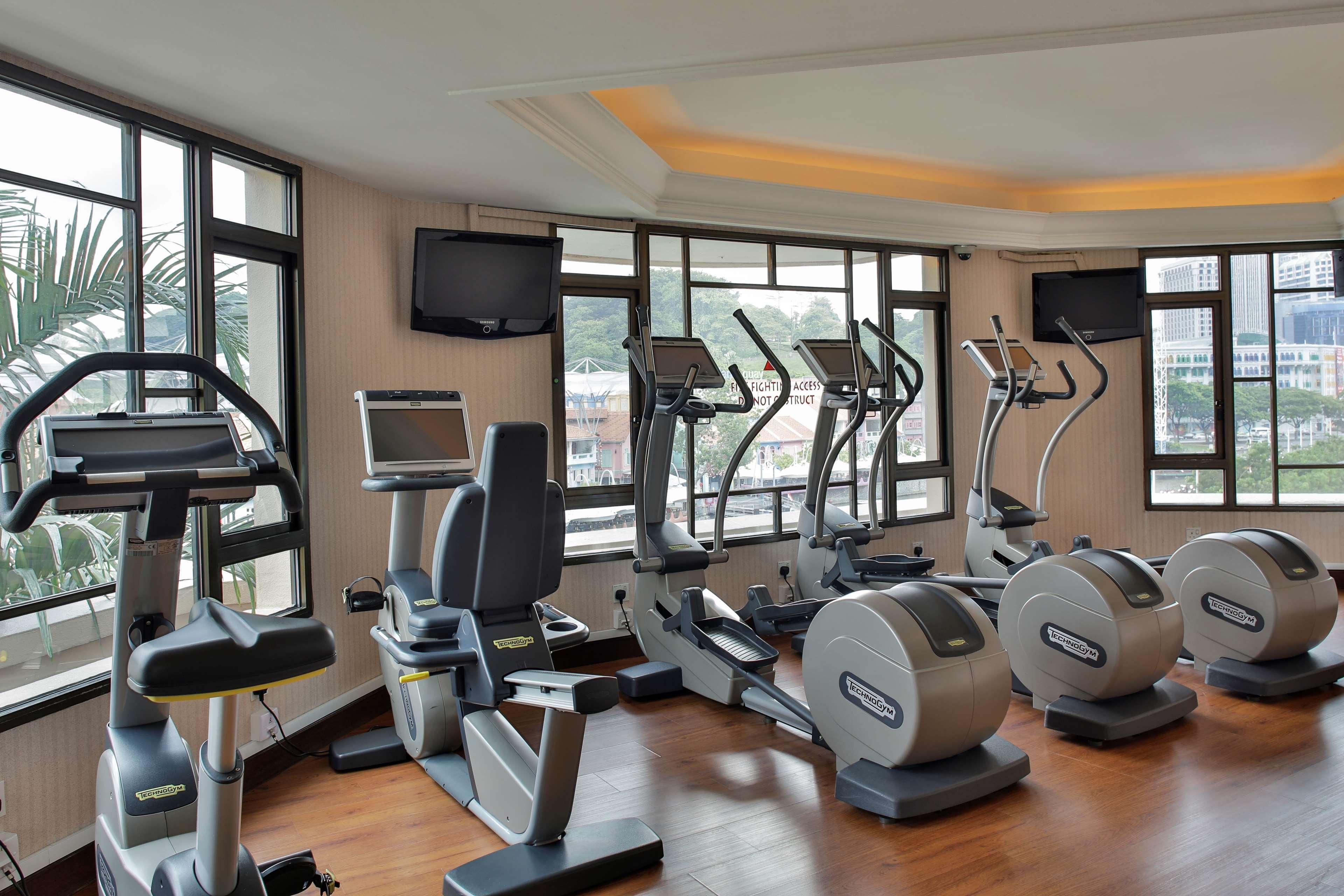 Paradox Singapore Merchant Court At Clarke Quay المظهر الخارجي الصورة The photo shows a fitness room equipped with various exercise machines. There are several elliptical machines and stationary bicycles positioned by large windows, allowing for natural light to fill the space. Additionally, there are two televisions m