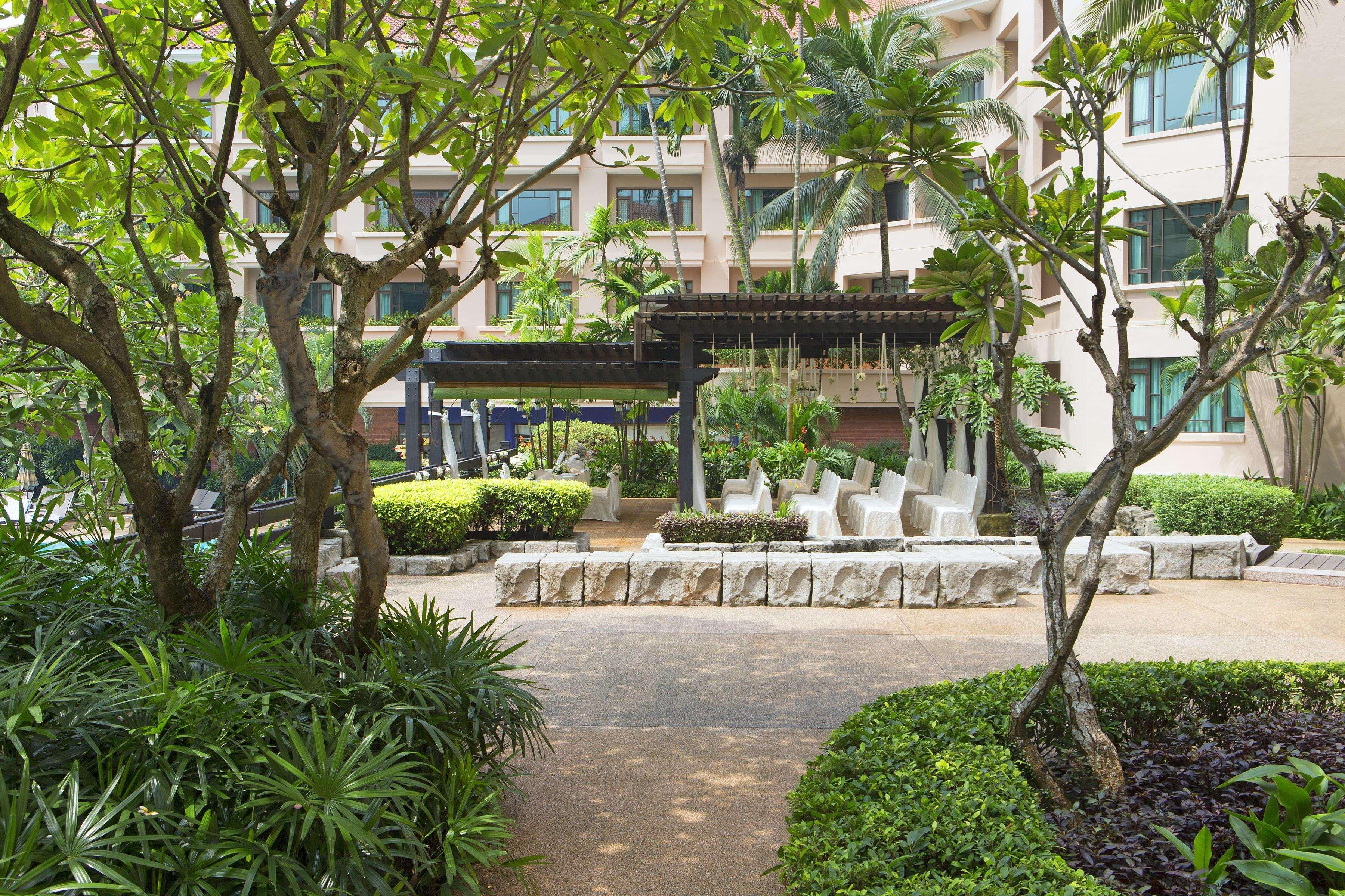 Paradox Singapore Merchant Court At Clarke Quay المظهر الخارجي الصورة The photo depicts a garden or courtyard area surrounded by lush greenery. There are several trees and vibrant plants, creating a serene environment. In the center, there seems to be a stone seating arrangement under a covered structure, likely meant 