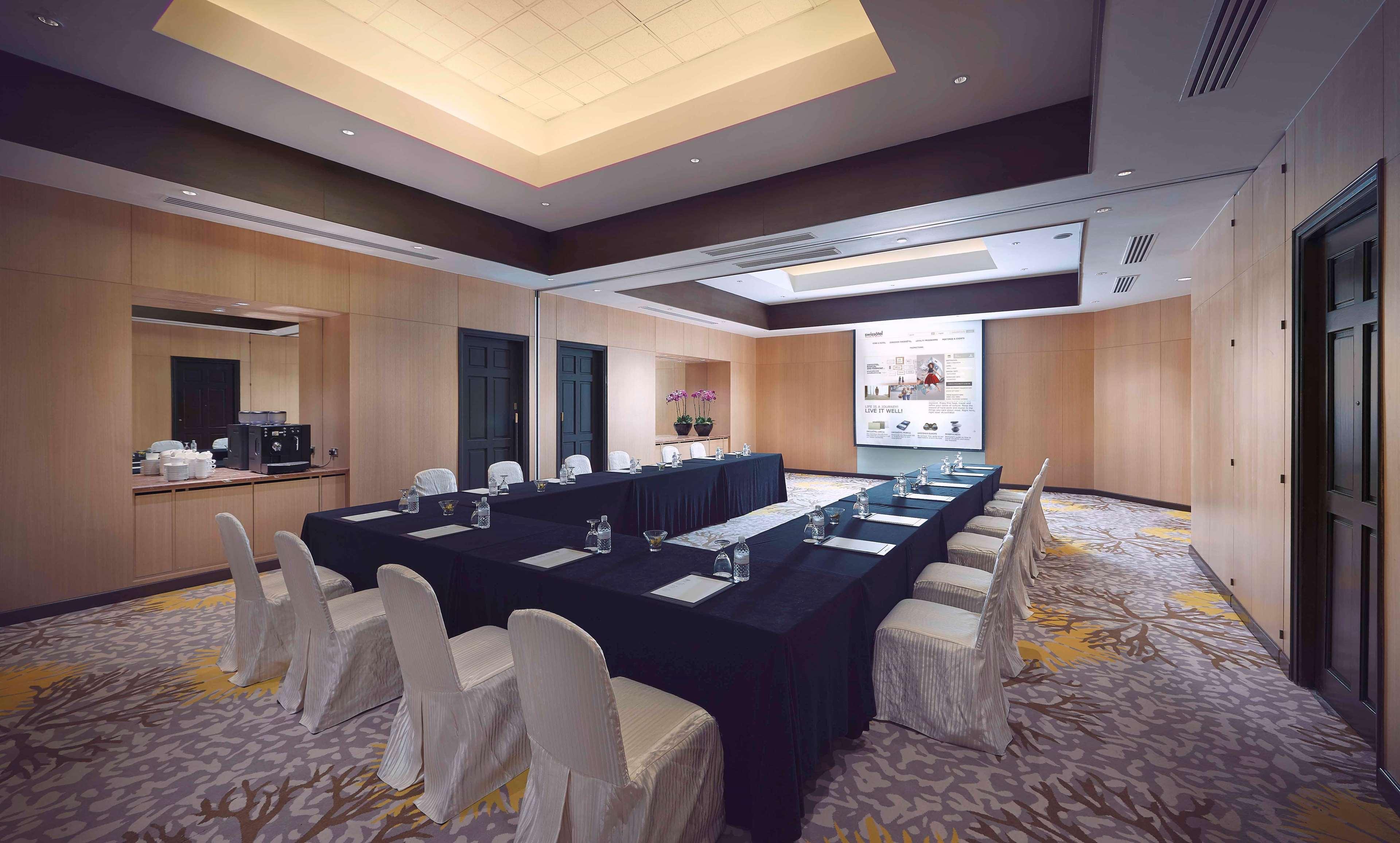 Paradox Singapore Merchant Court At Clarke Quay المظهر الخارجي الصورة The photo shows a conference room designed for meetings or presentations. It features a long rectangular table covered with a black tablecloth, surrounded by white chairs. There are glass water pitchers and glasses on the table. The room has wooden p
