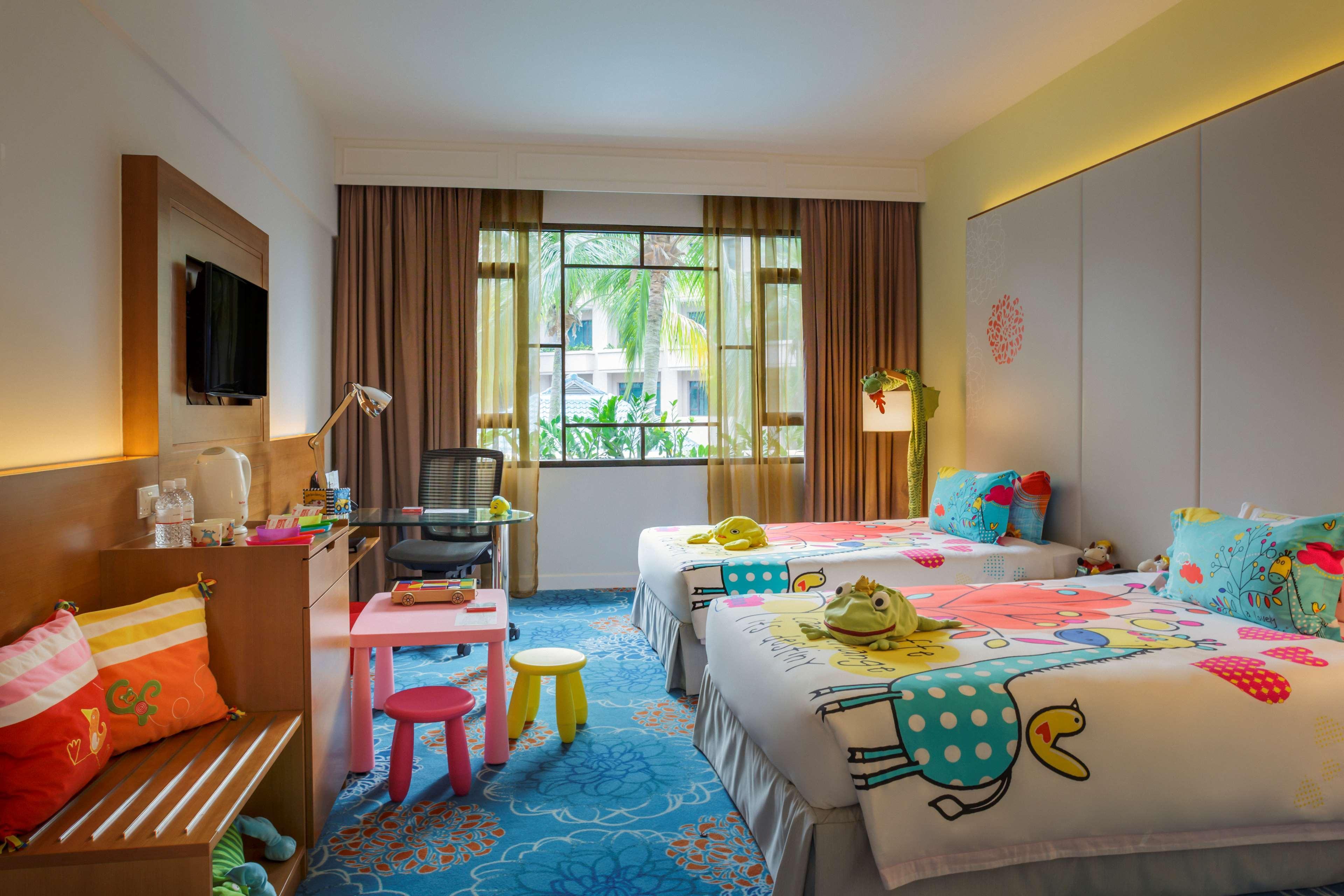 Paradox Singapore Merchant Court At Clarke Quay المظهر الخارجي الصورة The photo shows a brightly colored hotel room designed in a family-friendly style. There are two twin beds, each adorned with playful, colorful bedding featuring whimsical patterns. A small table with brightly colored stools is positioned nearby. A c