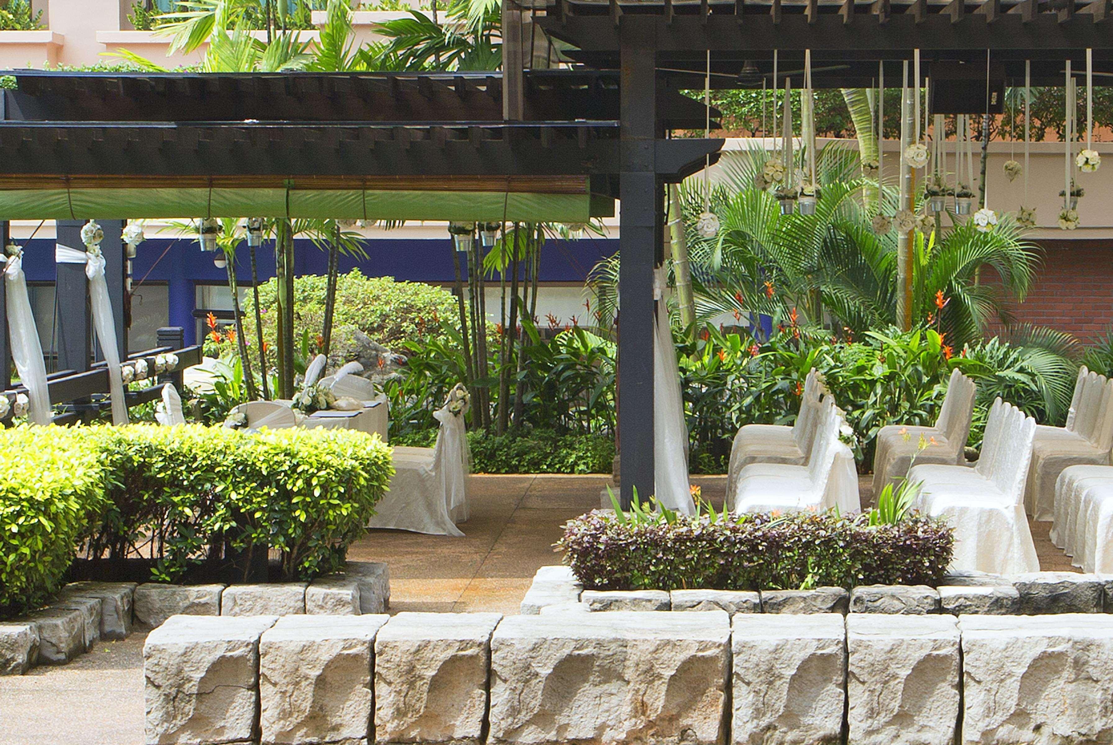 Paradox Singapore Merchant Court At Clarke Quay المظهر الخارجي الصورة The image shows a landscaped outdoor area featuring a mix of greenery and seating. There are several white chairs arranged in a relaxed setting under a shaded structure, surrounded by vibrant plants and bushes. In the background, there is a small tab