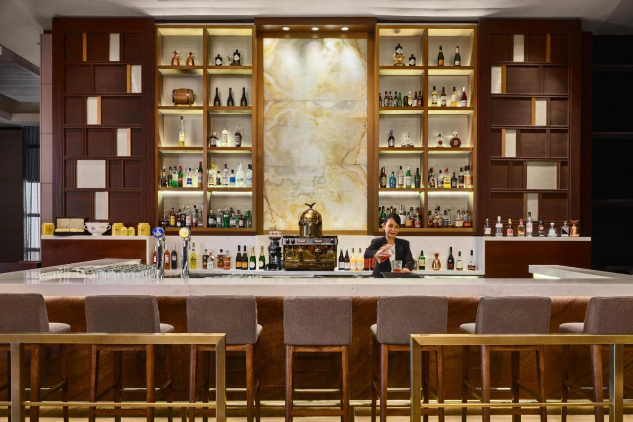 Paradox Singapore Merchant Court At Clarke Quay المظهر الخارجي الصورة The photo shows a well-designed bar area. The bar has a long counter with high stools arranged in front. Behind the bar, there is an elegant display of various bottles of spirits, arranged on shelves with a stylish backdrop. The shelves feature a com